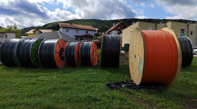 Auf einer freien Wiese stehen 8 Glasfaser-Kabeltrommeln unterschiedlicher Größe und Farben